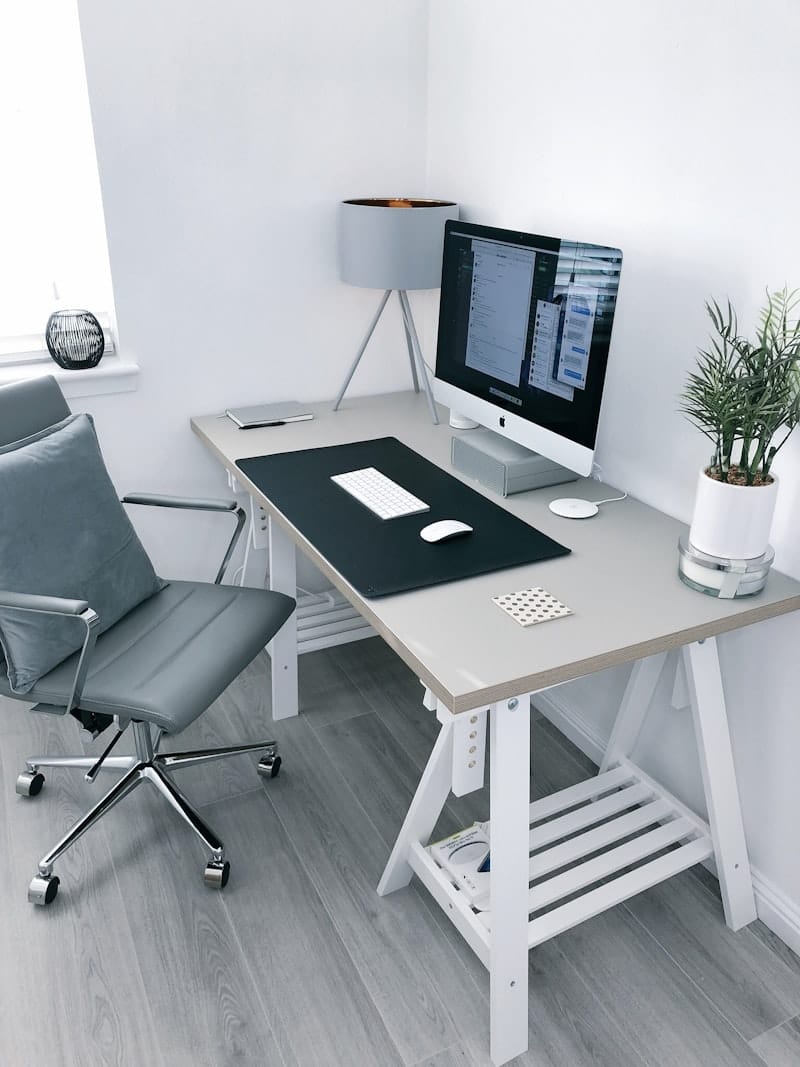 흰색 목재 책상에 iMac 모니터와 회색 사무용 의자가 놓인 홈오피스 셋업, 밝은 나무 바닥